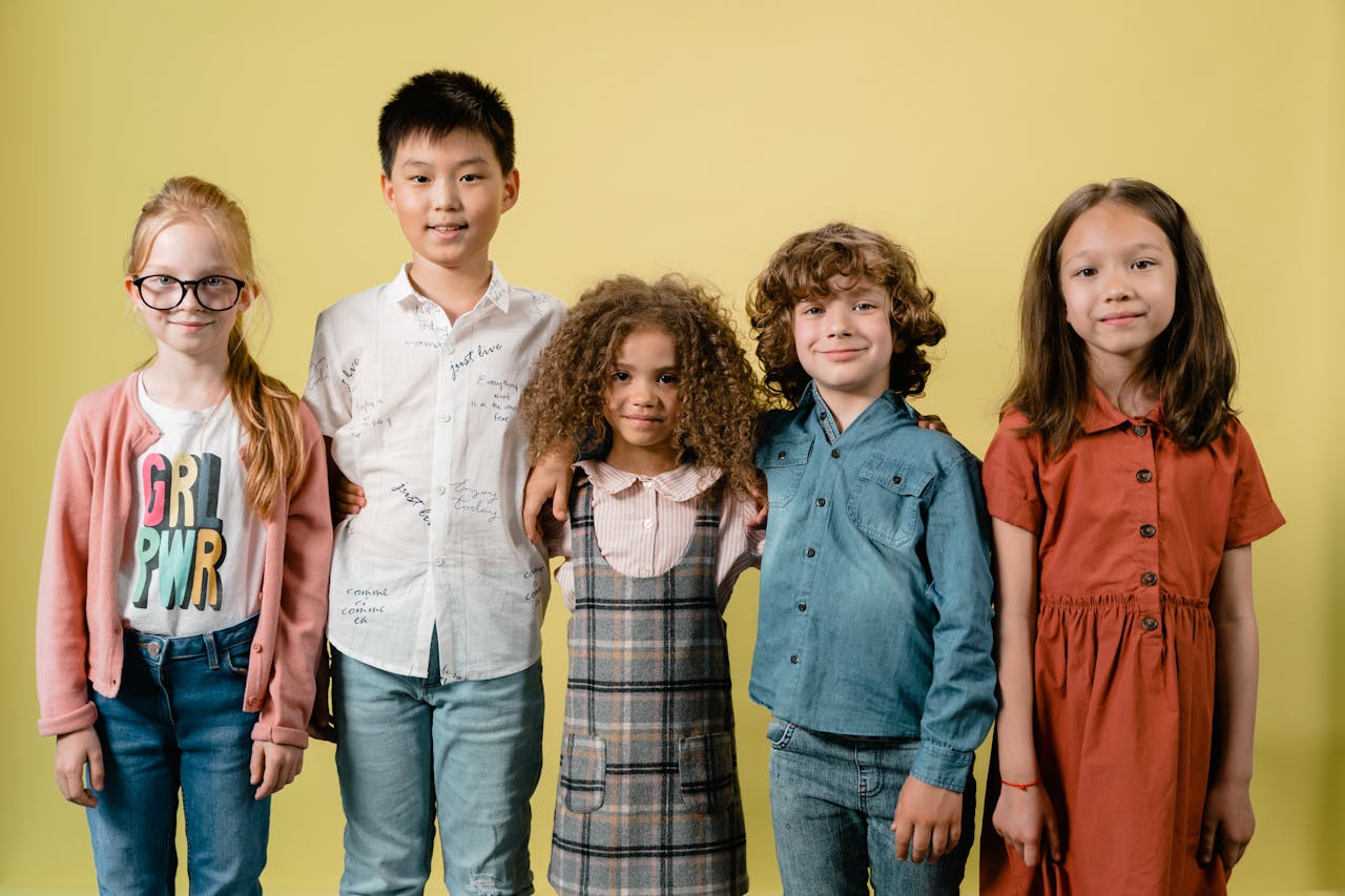 our-experience Five diverse children smiling against a yellow background in a studio setting.